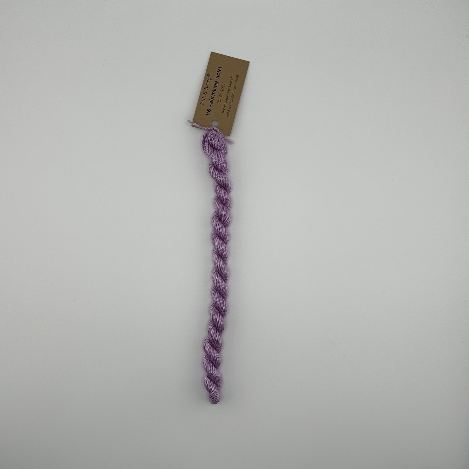 30 yard skein of silk & Ivory in the color 116 Shrinking Violet with brown tag laying flat on white background