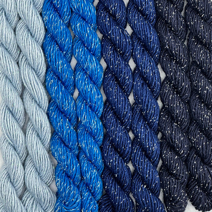 close-up of 8 skeins of Stardust Silk and Ivory needlepoint thread in four shades of blue including blue yonder 606, midnight 531, blue streak 592, and regatta 736, lying side by side.