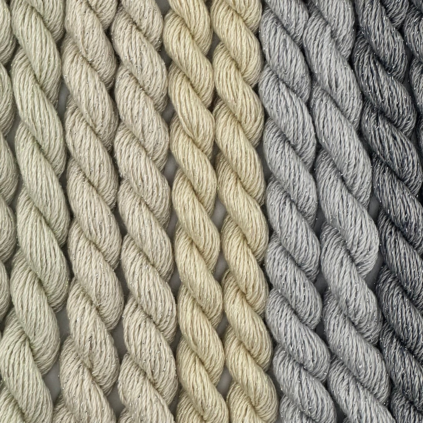 close-up of 9 skeins of Stardust Silk and Ivory needlepoint thread in five neutral shades including cucumber 599, candlelight 534, natural 501, pewter 717, and grey flannel 603, lying side by side.