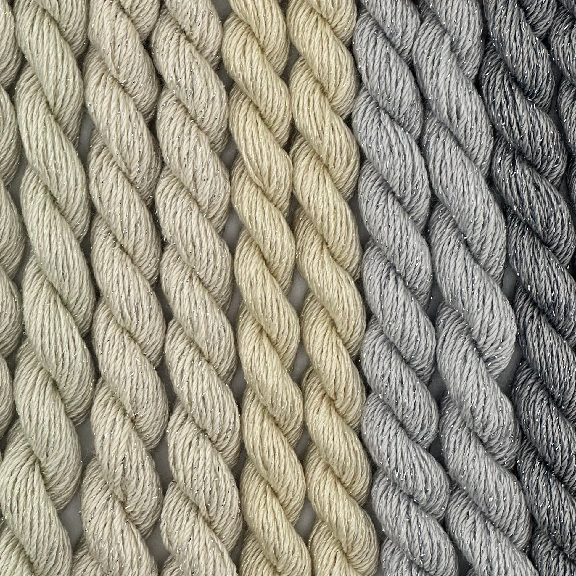 close-up of 9 skeins of Stardust Silk and Ivory needlepoint thread in five neutral shades including cucumber 599, candlelight 534, natural 501, pewter 717, and grey flannel 603, lying side by side.