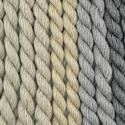 close-up of 9 skeins of Stardust Silk and Ivory needlepoint thread in five neutral shades including cucumber 599, candlelight 534, natural 501, pewter 717, and grey flannel 603, lying side by side.