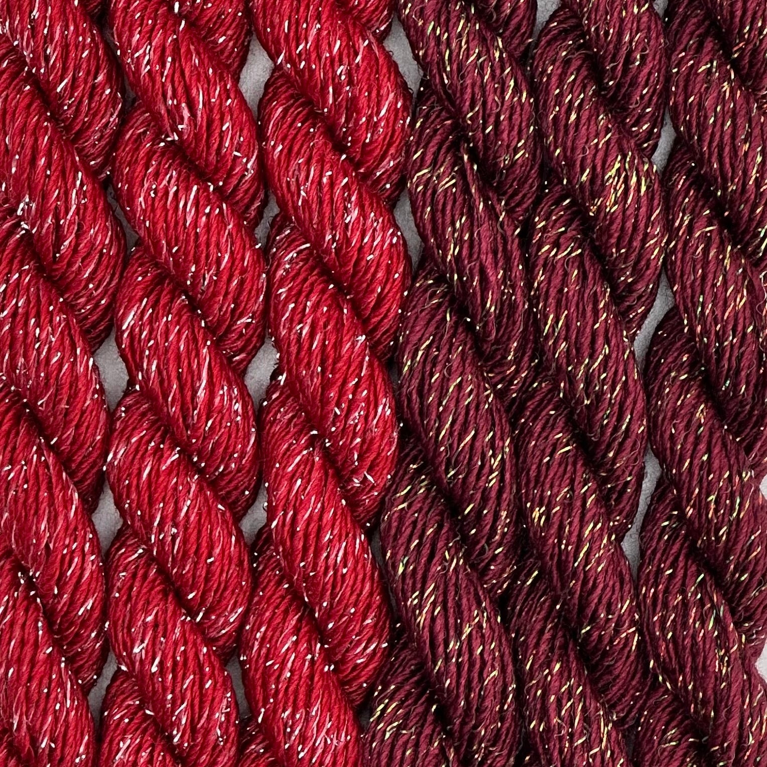 close-up of 6 skeins of Stardust Silk and Ivory needlepoint thread in  bordeaux 543 and ramblin rose 664 reds, lying side by side.