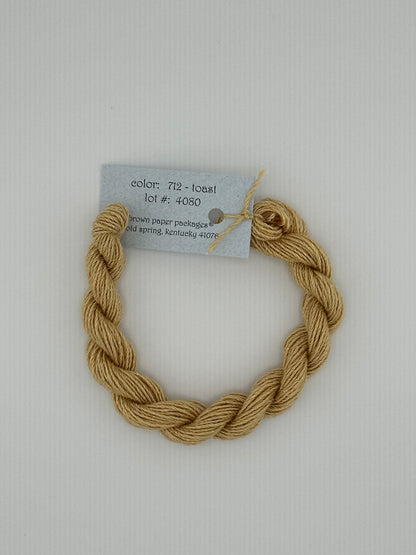 30 yard skein of Stardust Silk and Ivory needlepoint thread in Toast 712, with light blue label lying flat on white background