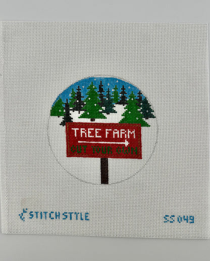 18 mesh needlepoint canvas featuring a design of a red 'Tree Farm' sign with a white arrow pointing right, set against a snowy pine tree landscape under a blue sky. The canvas is displayed on a white background with Stitch-Style branding and product code printed on the bottom.